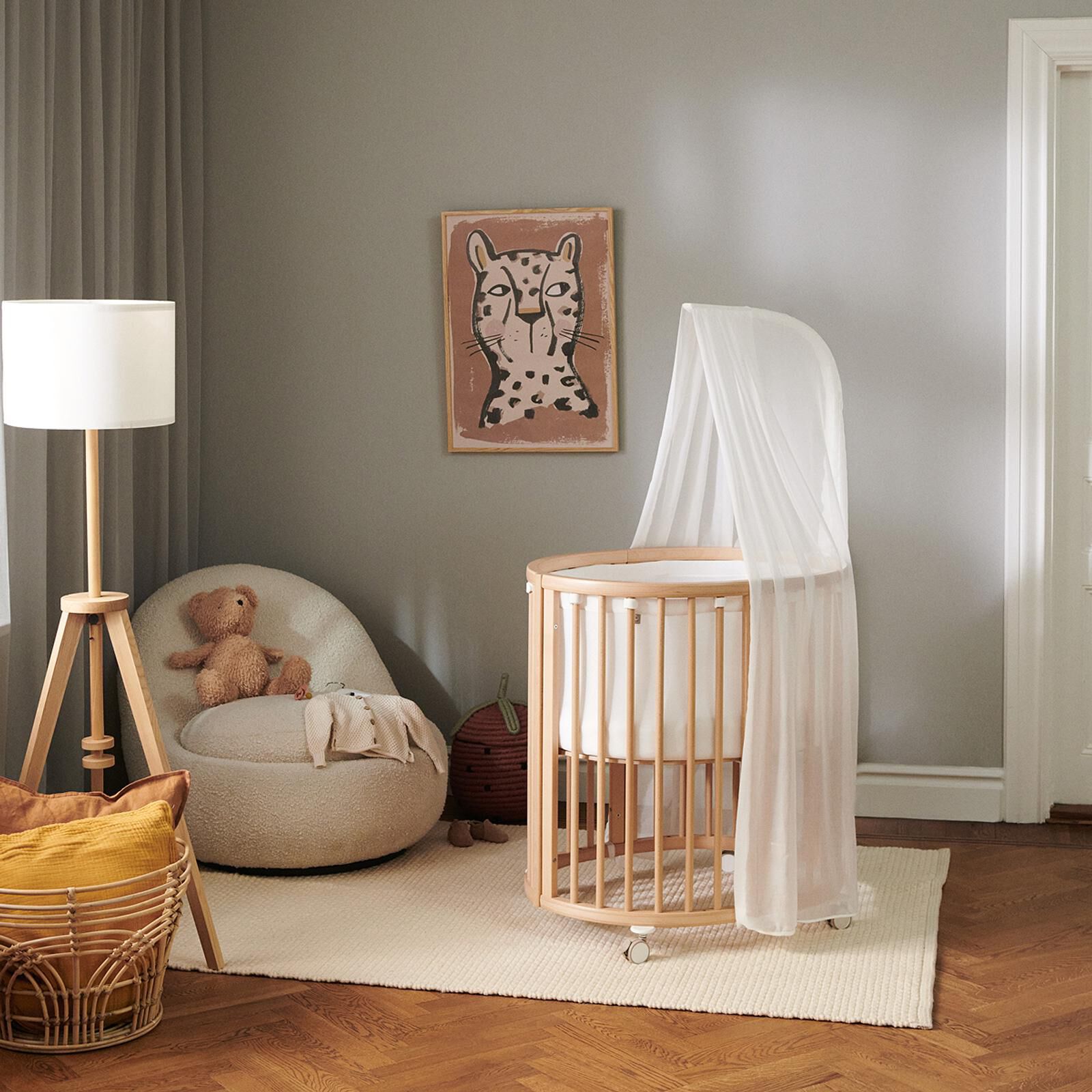 A cozy nursery with an oval wooden crib, a fluffy armchair with a teddy bear, and leopard wall art.