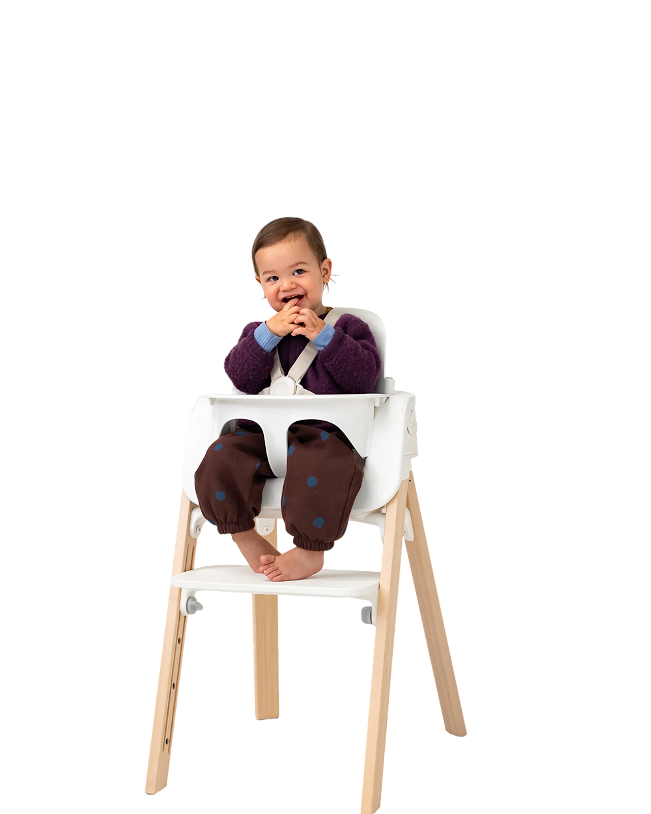 Een blije baby zit in een witte Tripp Trapp kinderstoel met natuurlijke houten poten en lacht naar de camera.