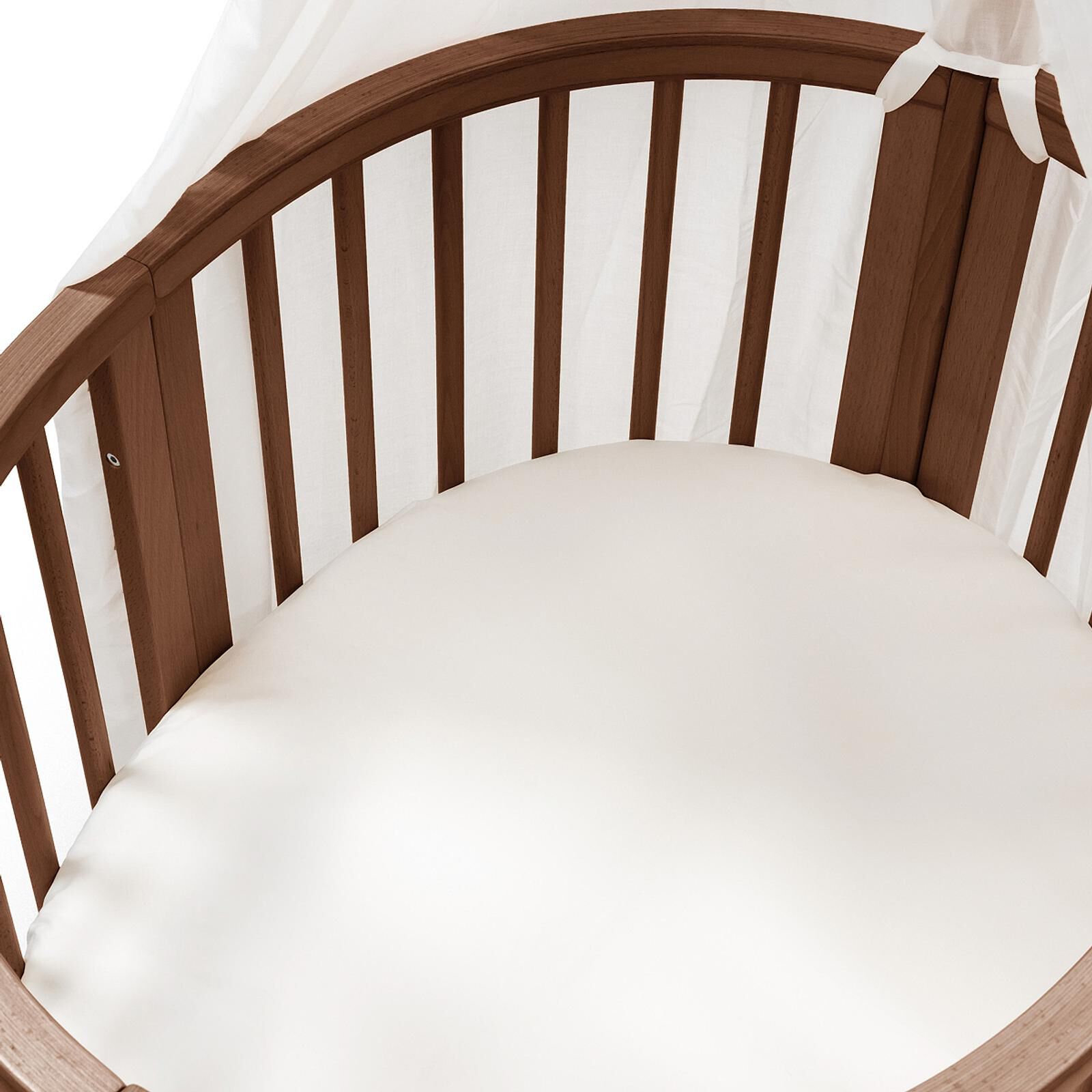 Oval wooden crib with white sheet and sheer canopy.