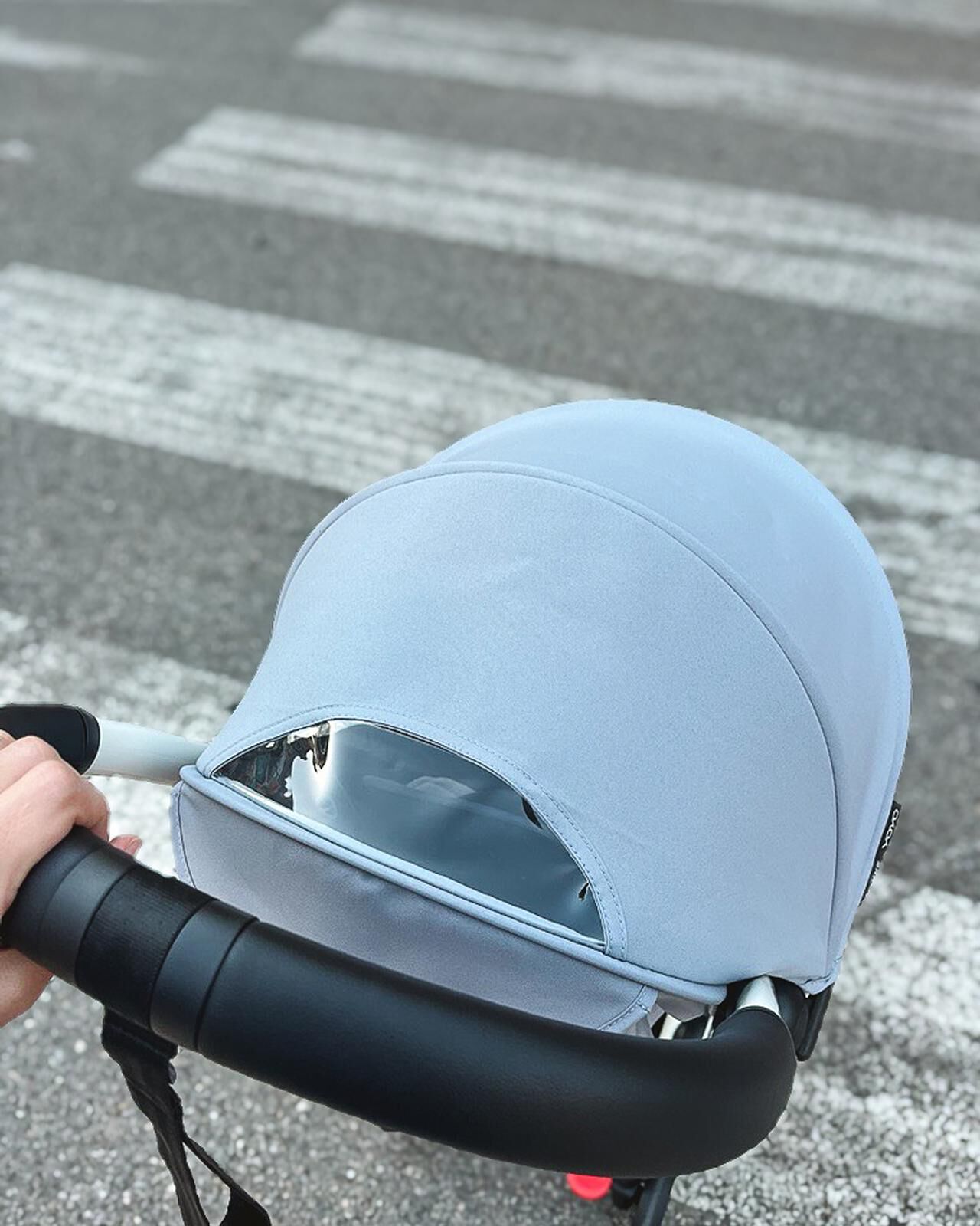 Hand som skjuter en ljusblå STOKKE YOYO barnvagn över ett övergångsställe.