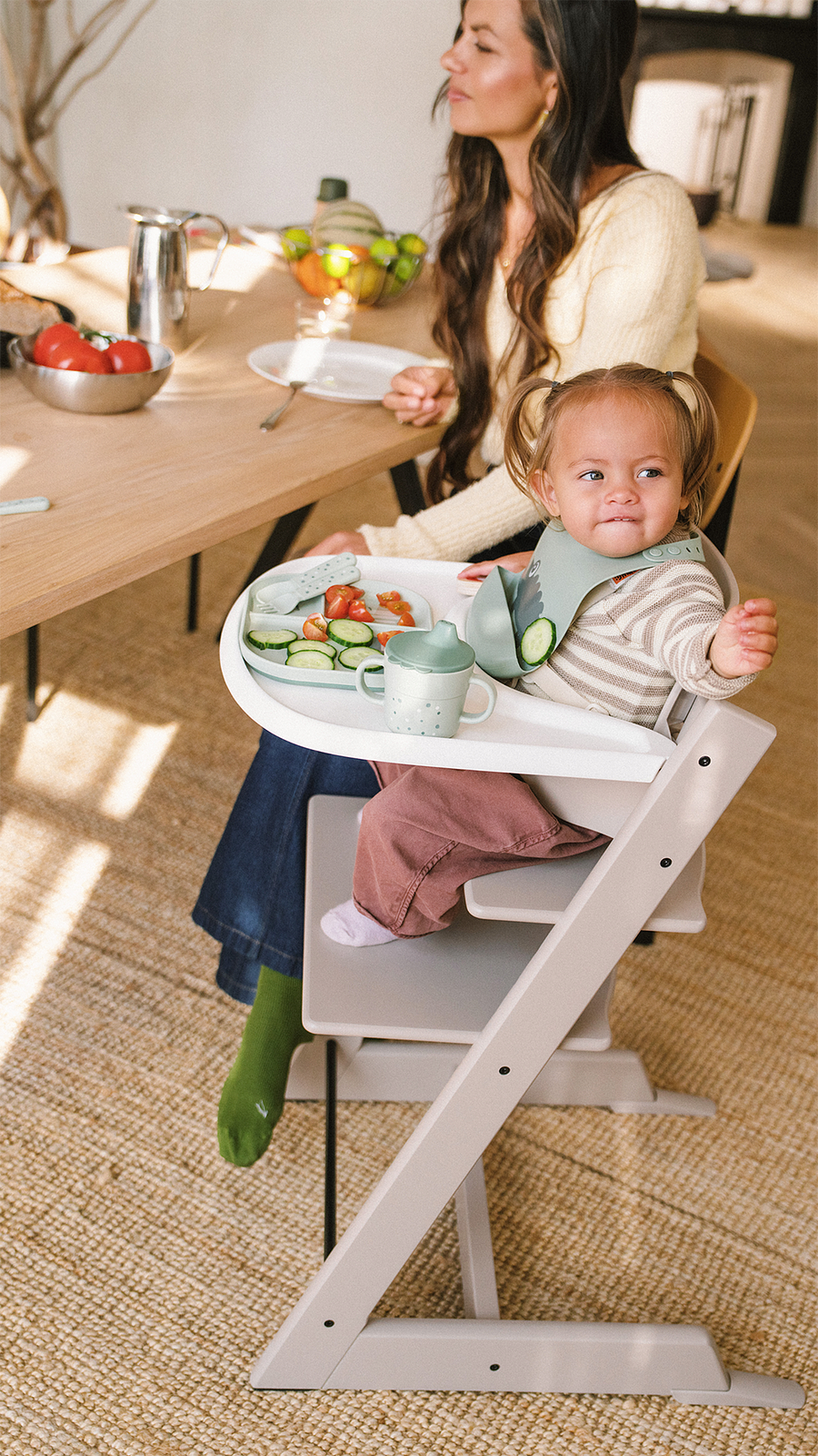 A baby in a Tripp Trapp high chair with a food tray sits next to an adult at a dining table.
