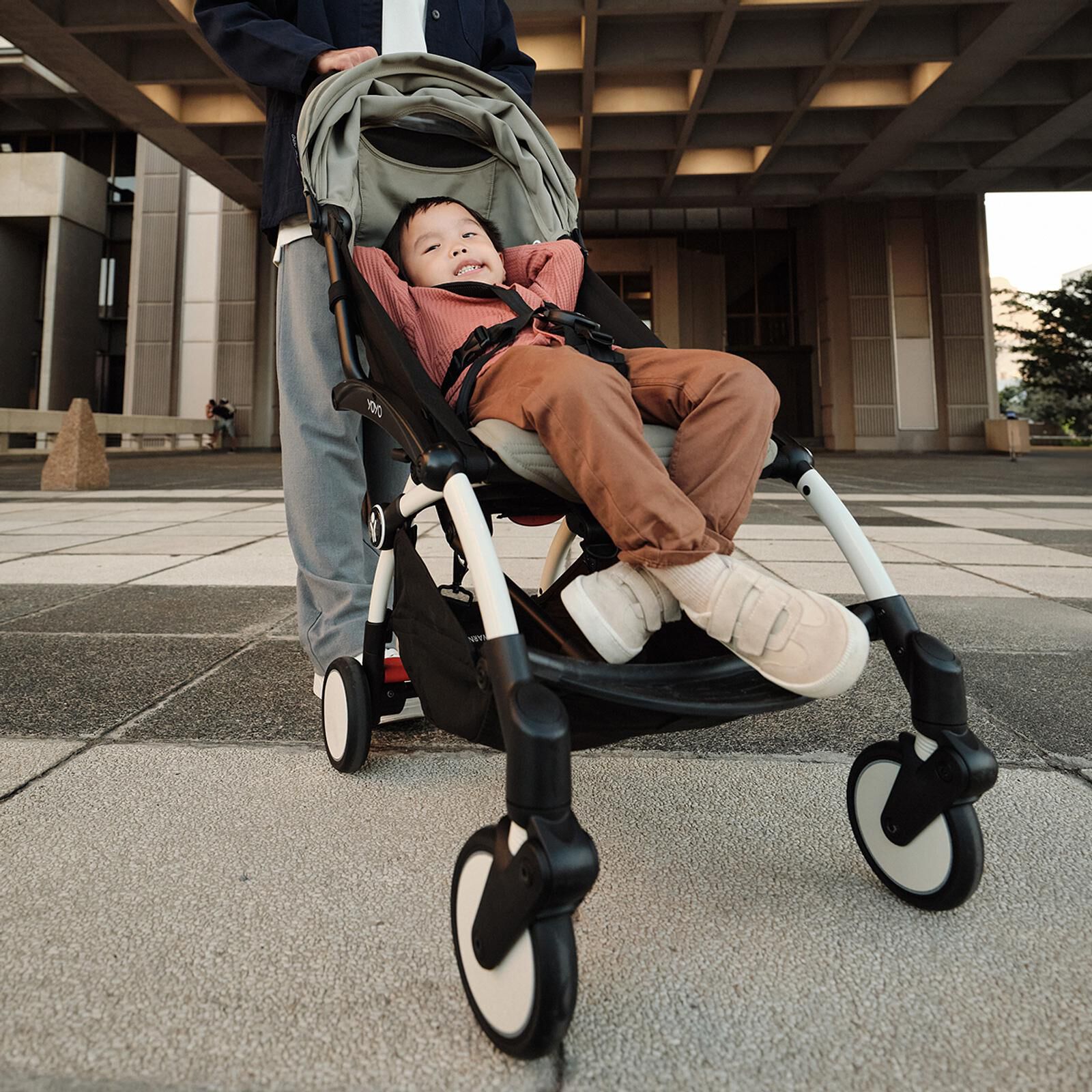 A smiling child relaxes in a STOKKE YOYO stroller, being pushed outdoors.