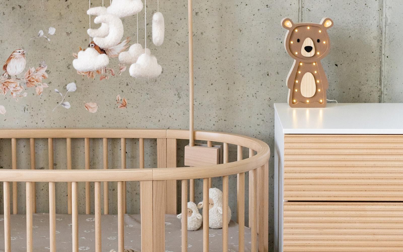 A cozy nursery with a wooden crib, cloud mobile, bird wall decor, and a bear night light.