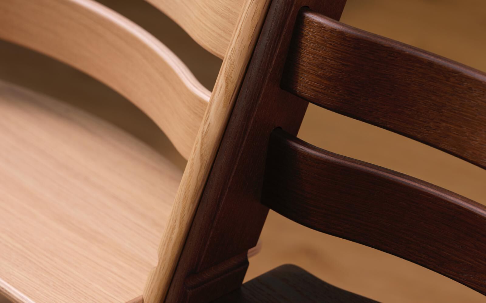 Two Tripp Trapp chairs, one light wood and one dark wood, side-by-side.