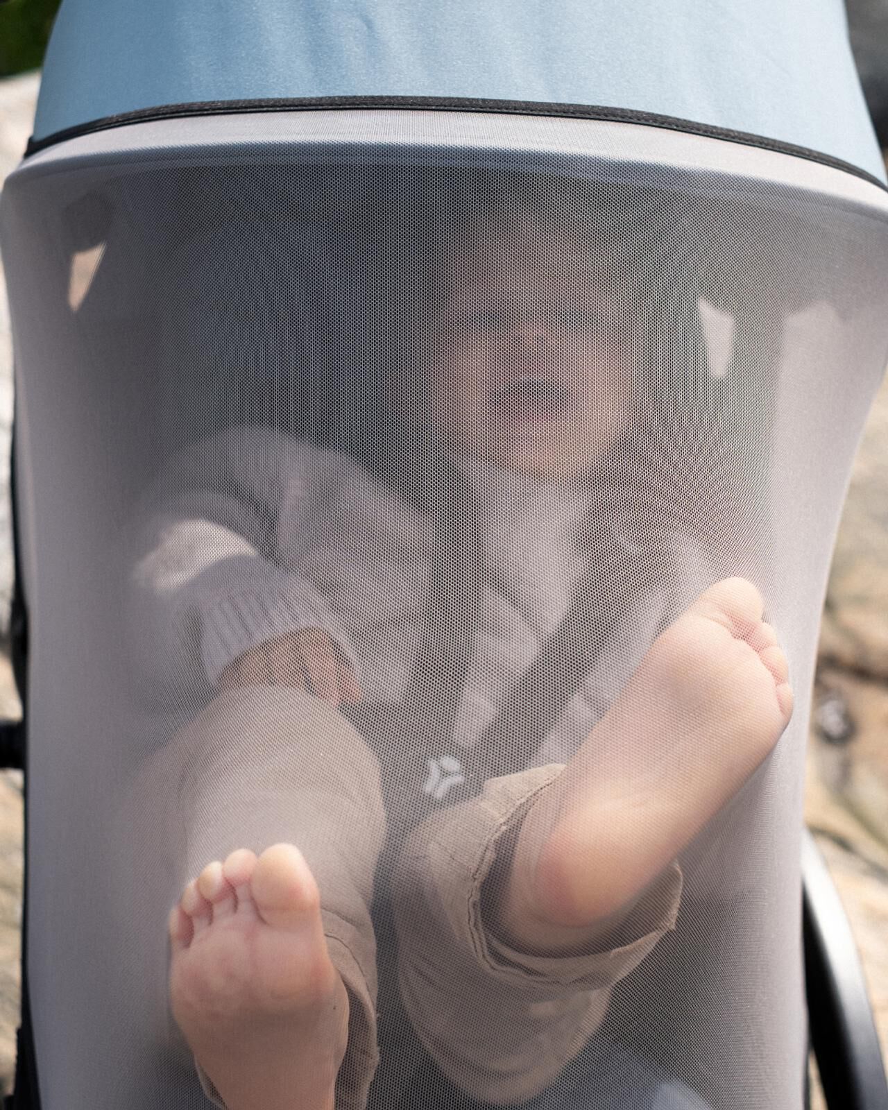 Baby in a STOKKE YOYO stroller with a mesh cover, showing bare feet.