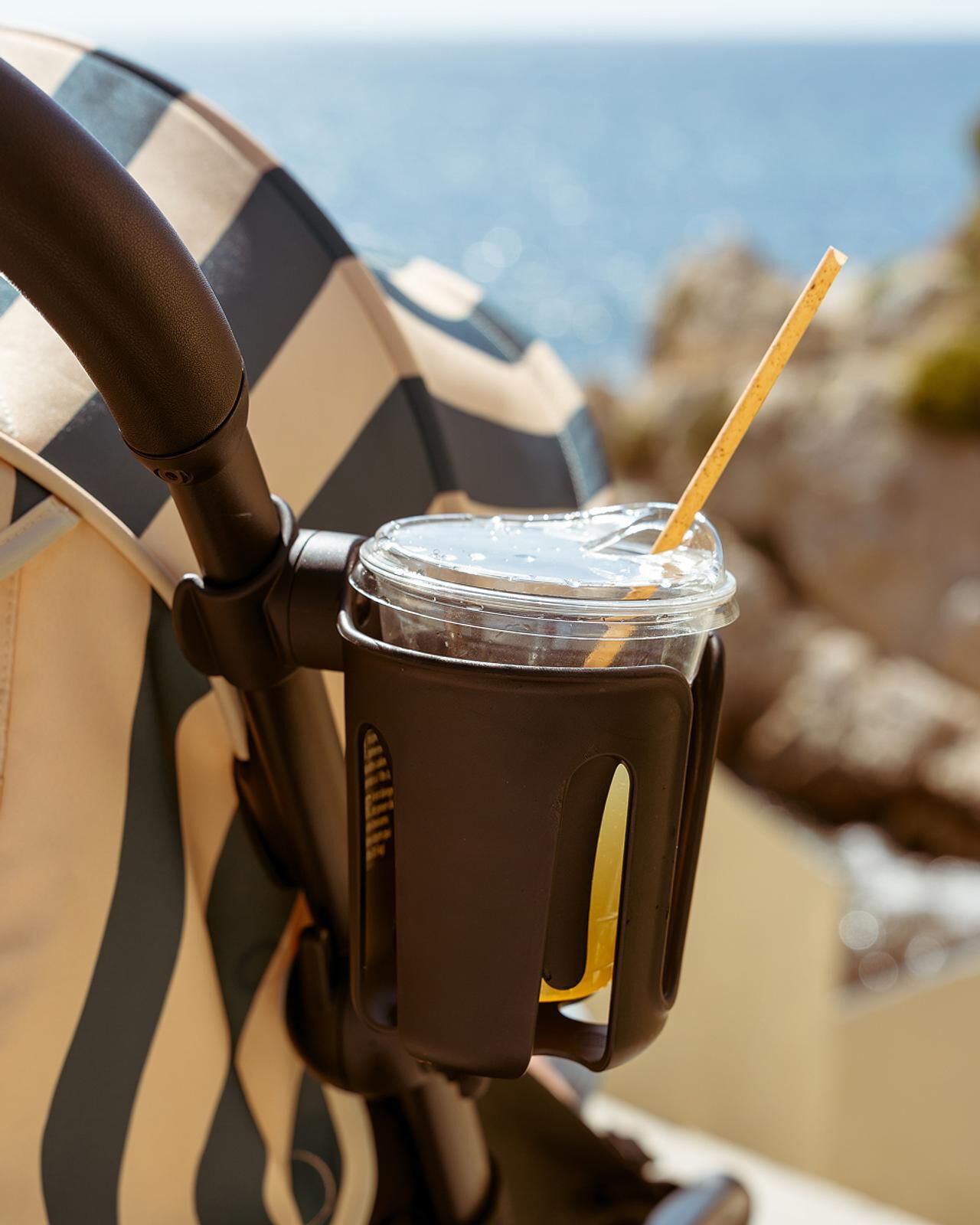 STOKKE YOYO stroller with a cup holder holding a drink and straw, with the sea in the background.