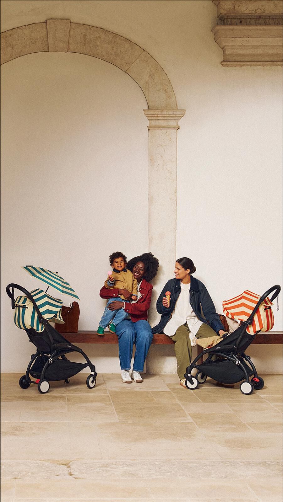 Deux femmes et un enfant dégustent une glace sur un banc, flanqués de deux poussettes STOKKE YOYO.