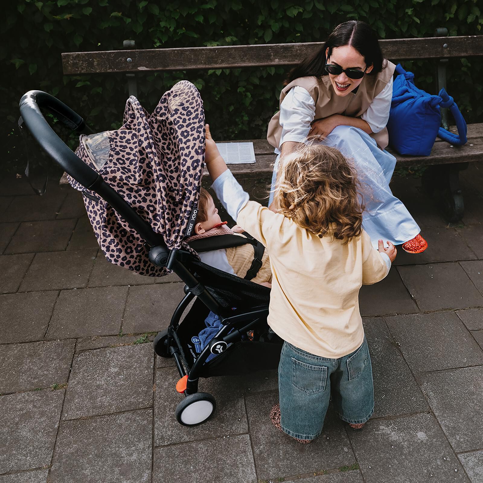 Woman smiles at children, one in a STOKKE YOYO stroller with leopard print canopy.