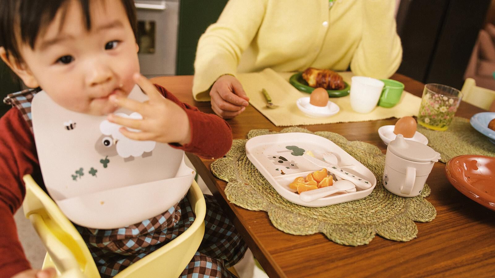 Een kind in een Tripp Trapp kinderstoel eet sinaasappelpartjes aan tafel met een volwassene.