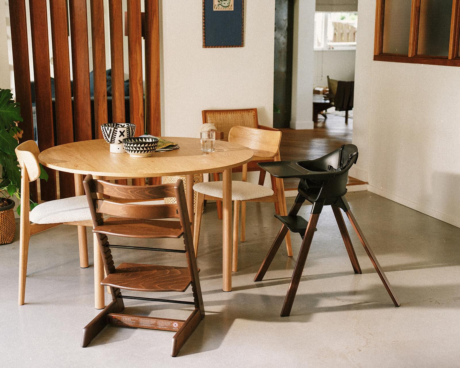 A dark brown Tripp Trapp chair and a black high chair next to a dining table.