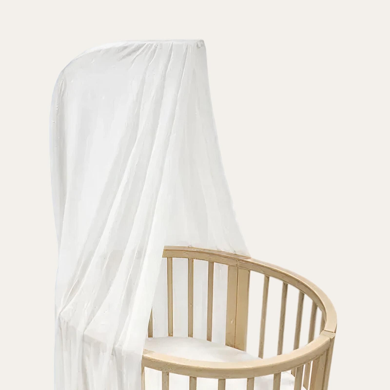 Oval STOKKE Sleepi crib with white mattress and sheer white canopy.