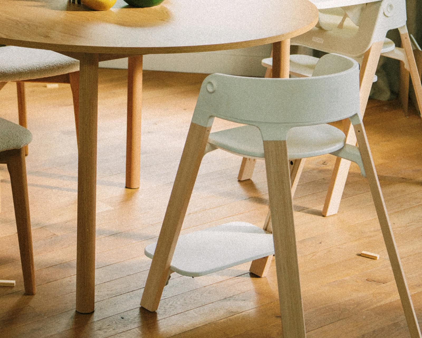 Une chaise moderne gris clair et une chaise haute blanche à côté d'une table à manger ronde en bois.