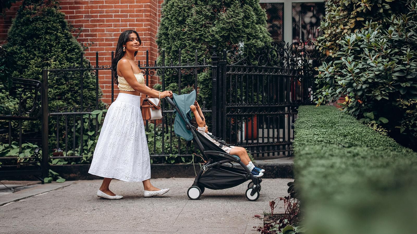 yoyo_hero-image_desktop_jpg Frau schiebt Kind in einem STOKKE YOYO Kinderwagen auf einem Bürgersteig in der Stadt.