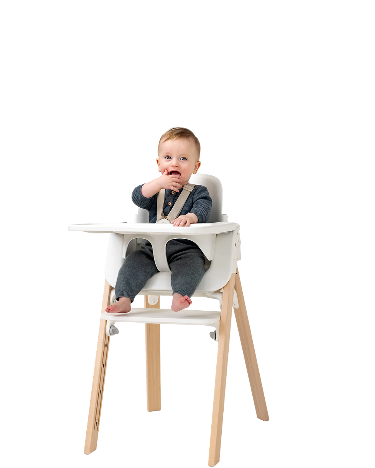 Un bambino è seduto su un seggiolone Tripp Trapp bianco, con la mano vicino alla bocca.