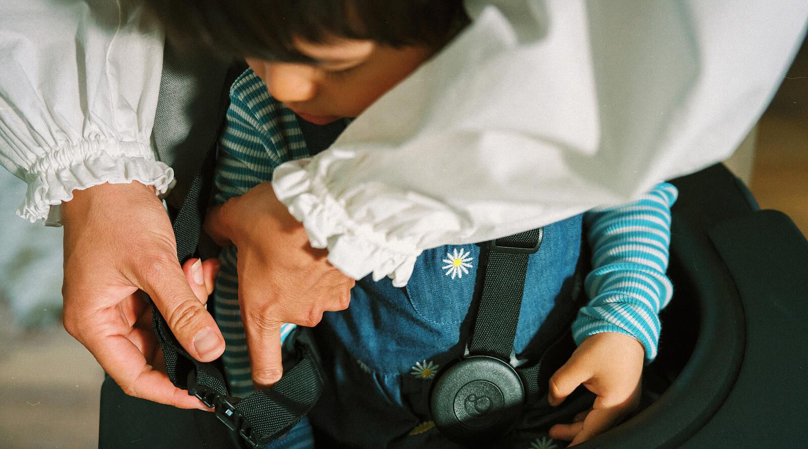 Een volwassene gespt een kind vast in het STOKKE YOYO kinderwagenharnas.