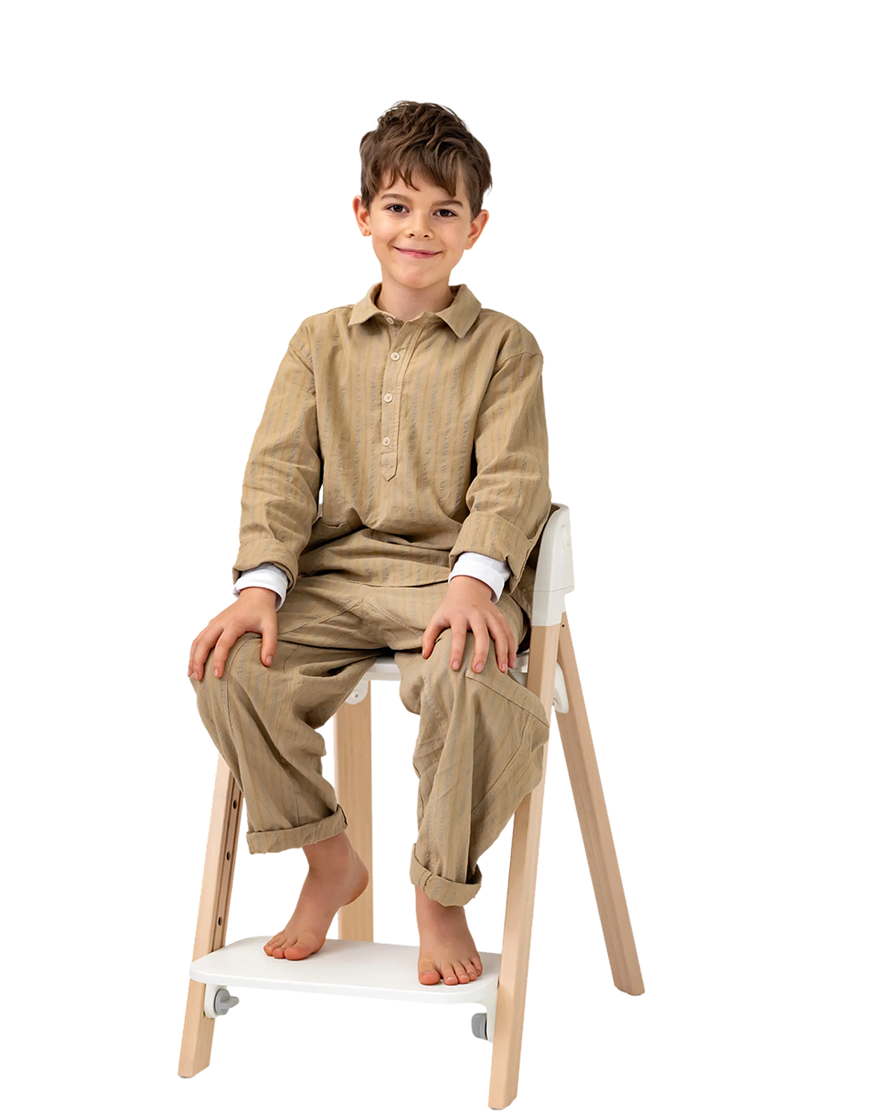 Smiling boy sits barefoot in a light wood and white high chair.