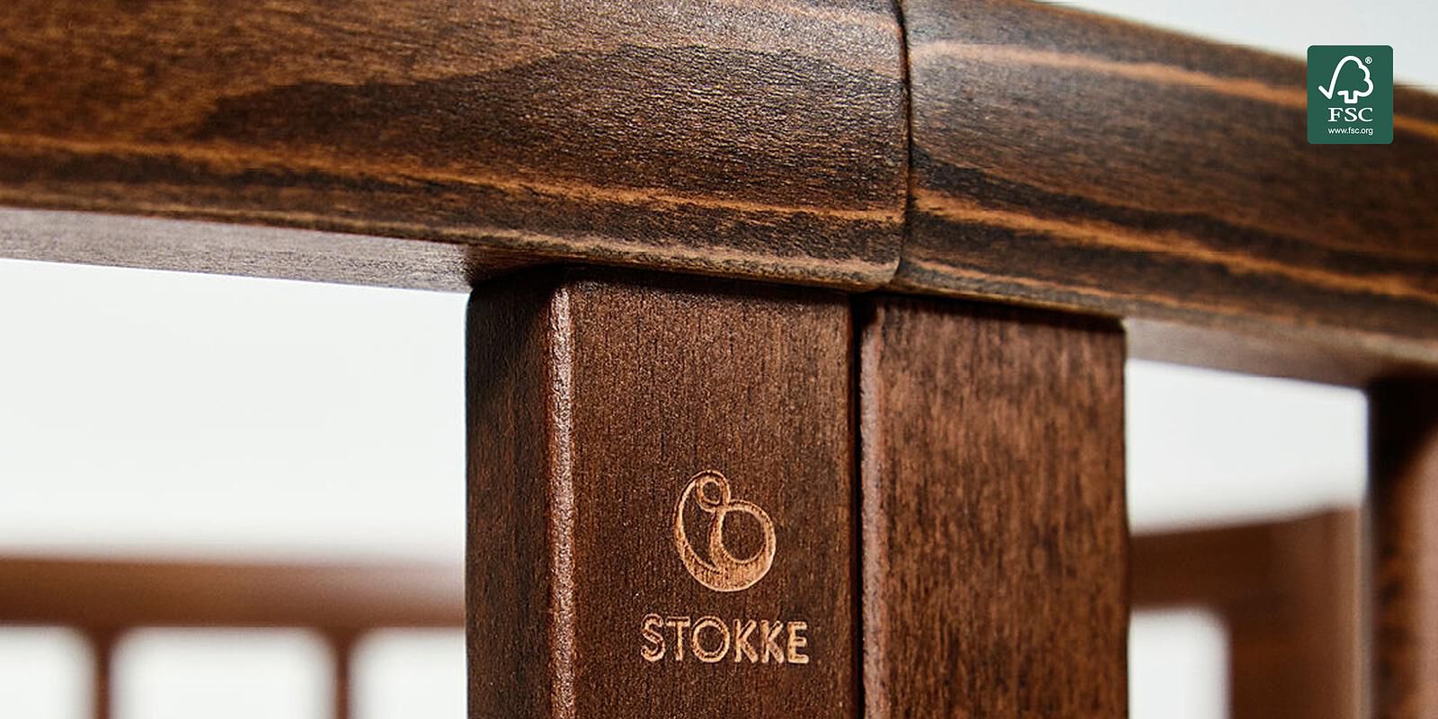 Gros plan d'une barrière de lit de bébé en bois brun foncé avec un logo Stokke gravé et une certification FSC.