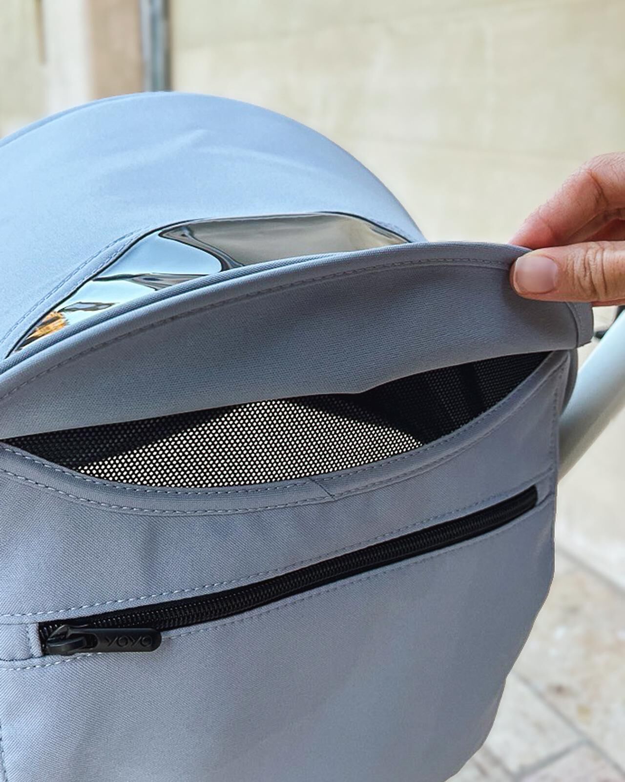 Hand öffnet graues STOKKE YOYO Kinderwagenverdeck, das ein Netzlüftungsfenster zeigt.