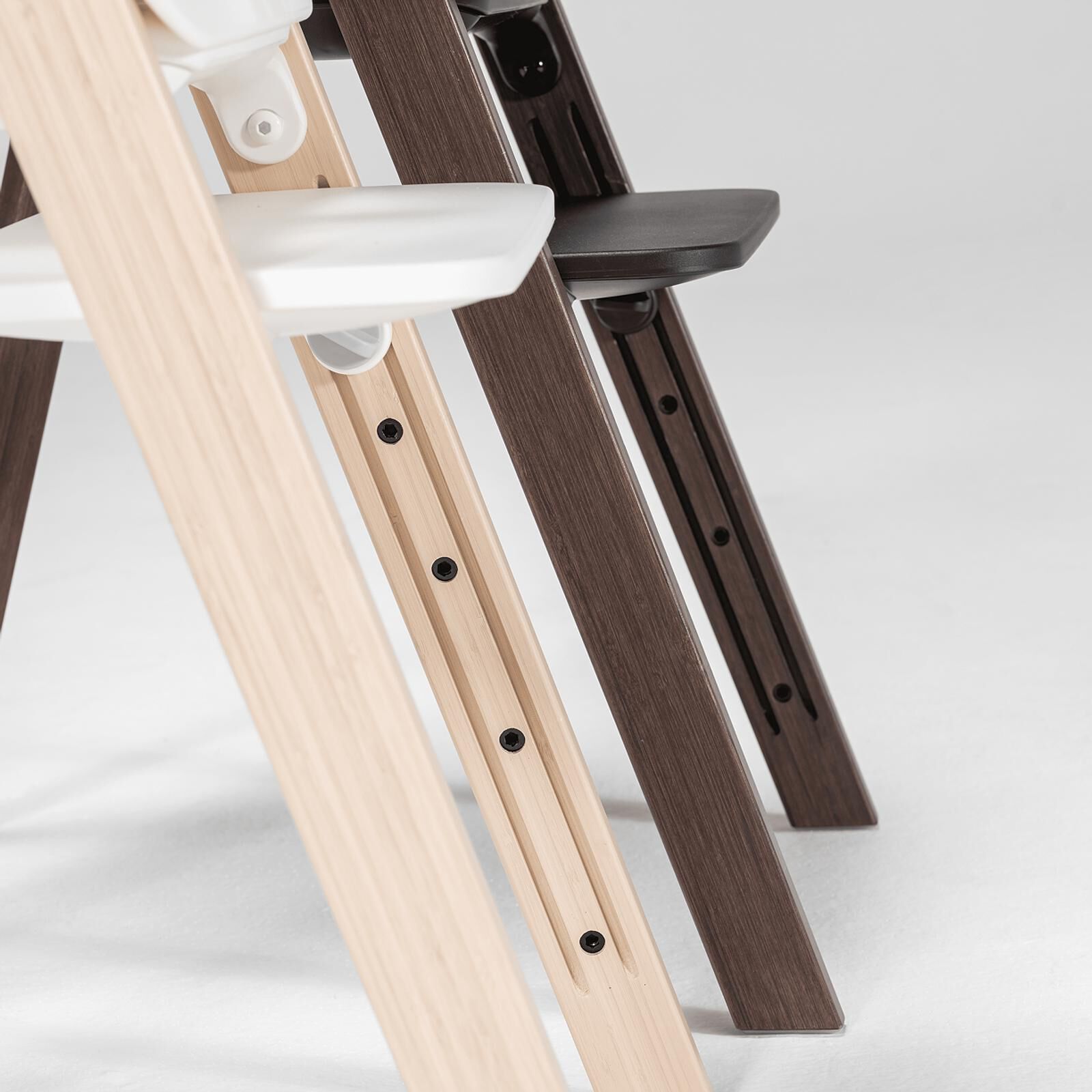 Primo piano di un seggiolone Tripp Trapp in legno naturale con Baby Set bianco e di una sedia Tripp Trapp in legno scuro.