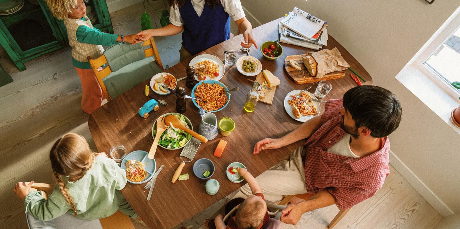 A family eats spaghetti at a table with two Tripp Trapp chairs and one Tripp Trapp high chair.