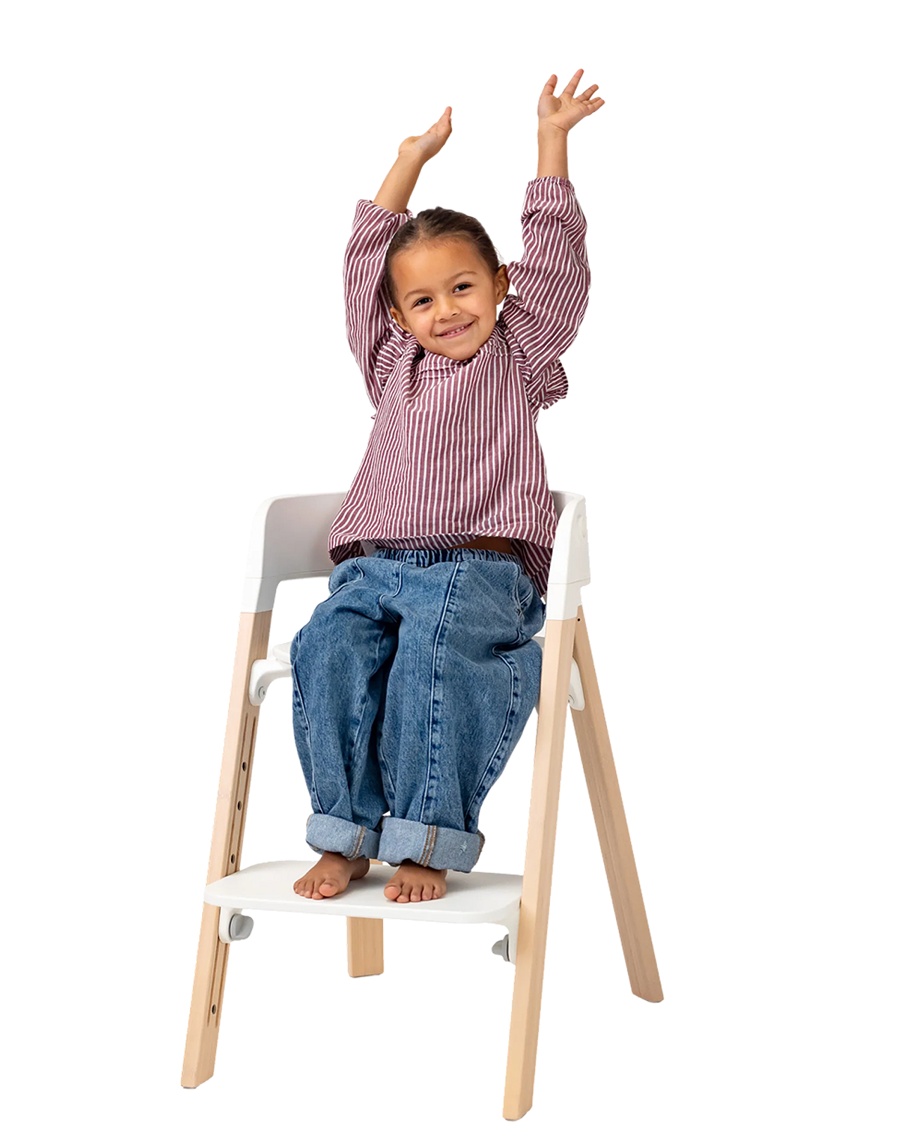 A smiling child with arms raised sits in a white and wood high chair.
