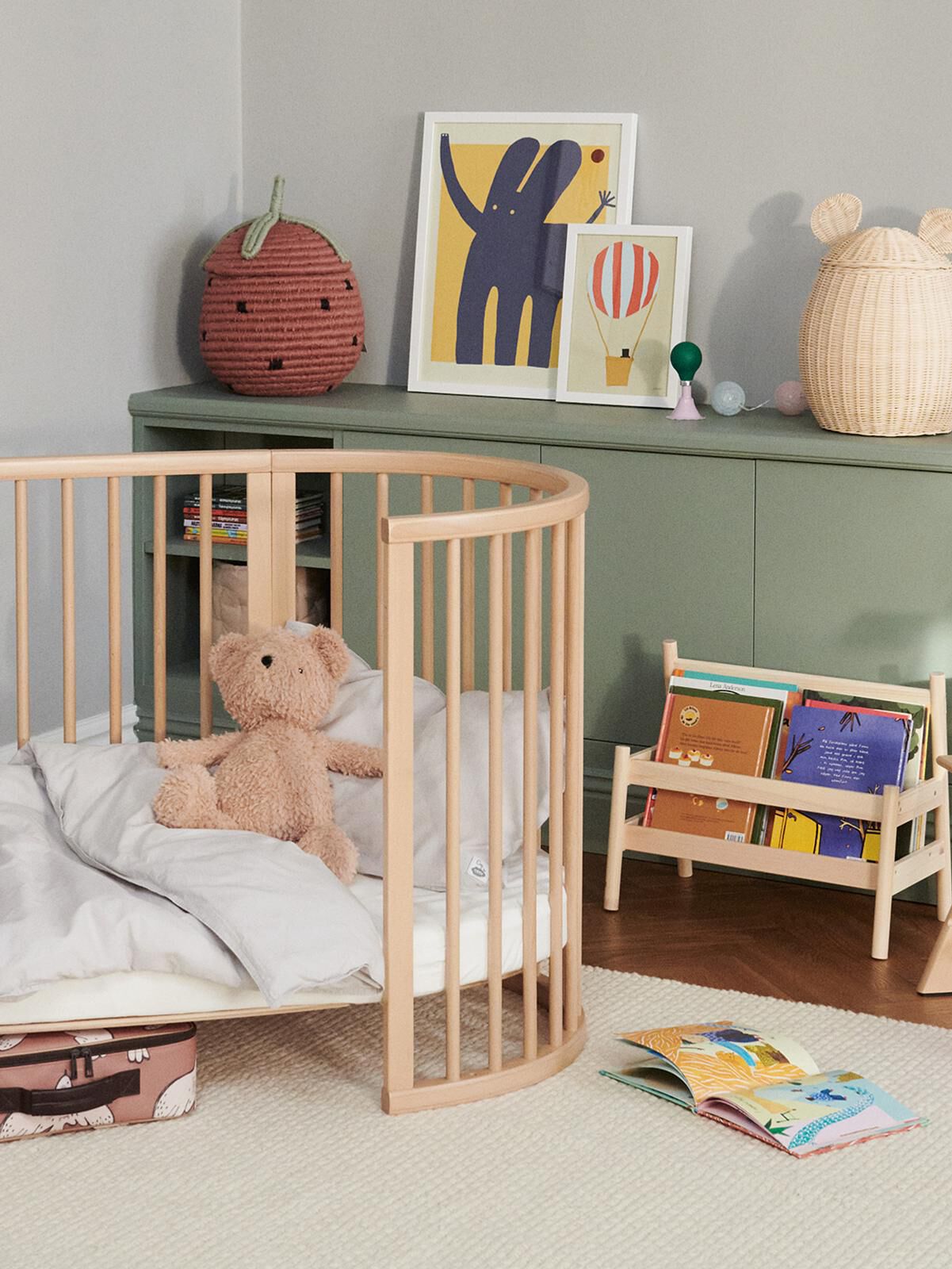 A cozy nursery with an oval wooden crib, teddy bear, children's books on a shelf, and playful decor.