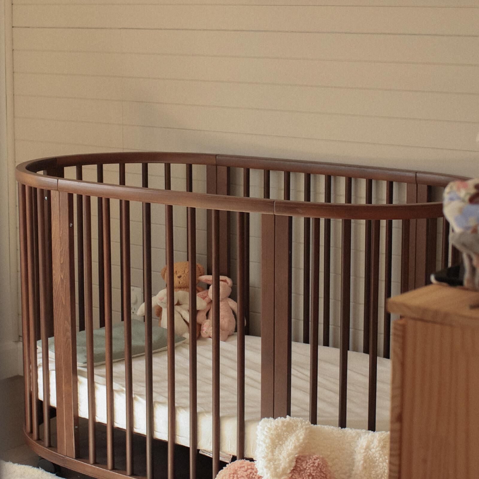 Lit bébé STOKKE Sleepi en bois foncé avec un matelas et plusieurs animaux en peluche à l'intérieur.