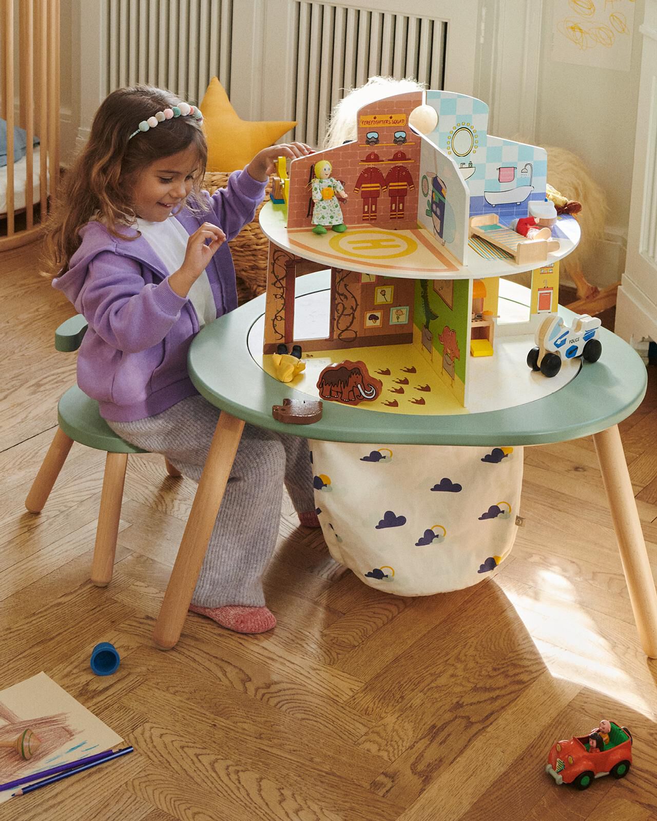 A girl plays with a multi-level dollhouse playset at a green children's table.
