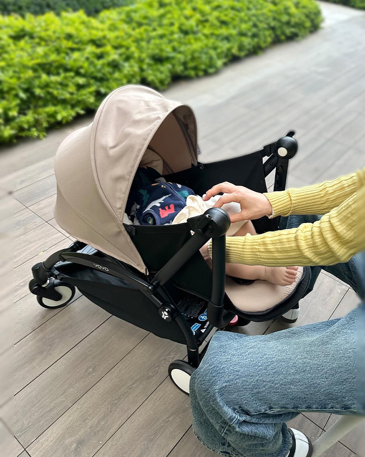 Person som tar hand om bebis i en beige YOYO-barnvagn på en träterrass.