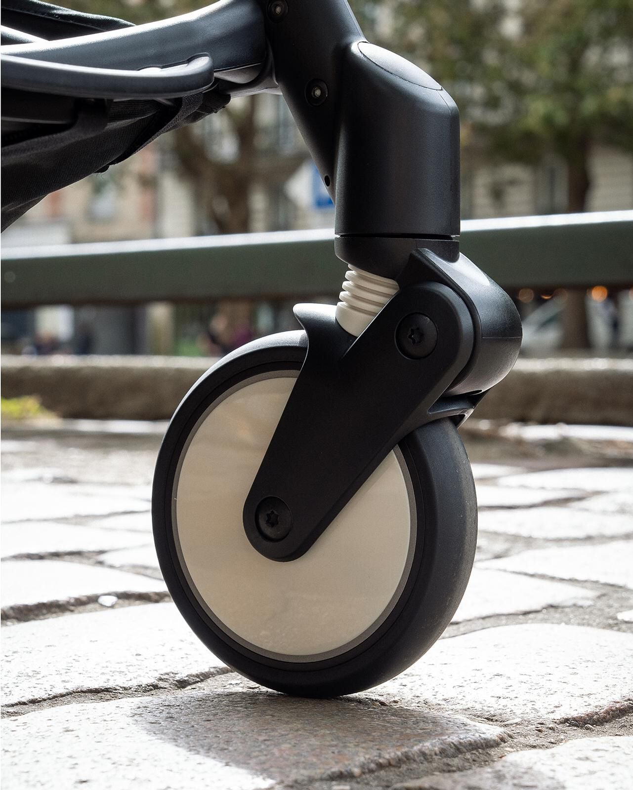 Primer plano de una rueda y la suspensión de un cochecito STOKKE YOYO en una calle pavimentada.