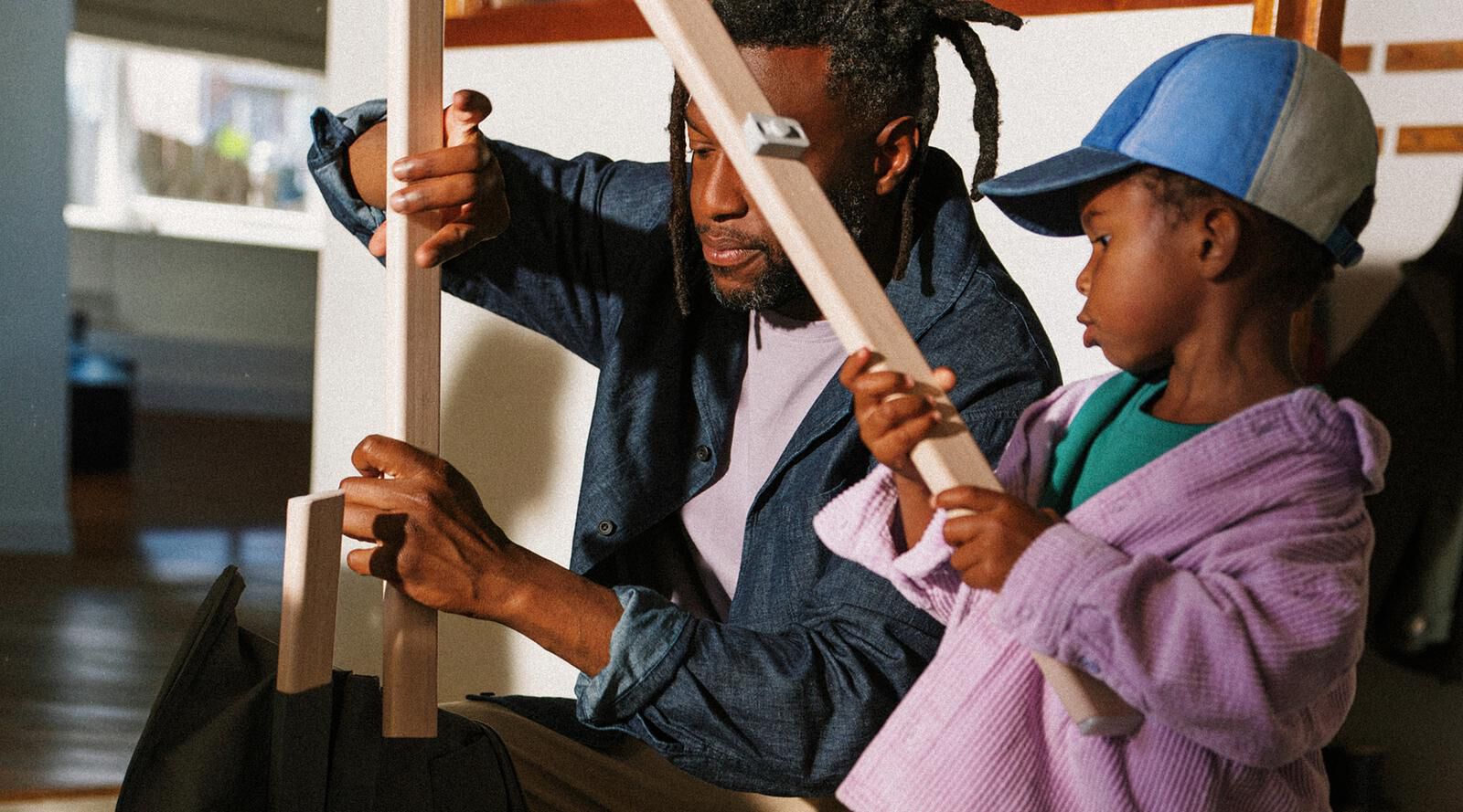 A man and child assemble a STOKKE YOYO stroller, holding its wooden frame parts.