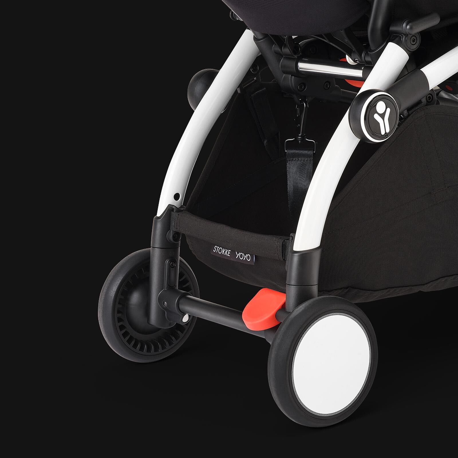 Close-up of a STOKKE YOYO stroller's white frame, black basket, and wheels with orange brake.