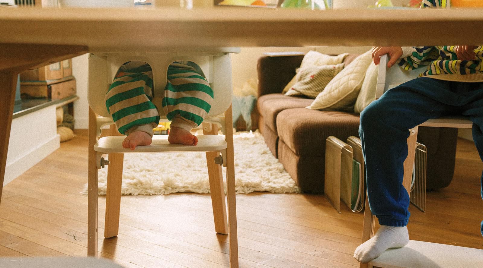 Due bambini sono seduti a un tavolo su sedie Tripp Trapp, uno su un seggiolone Tripp Trapp.