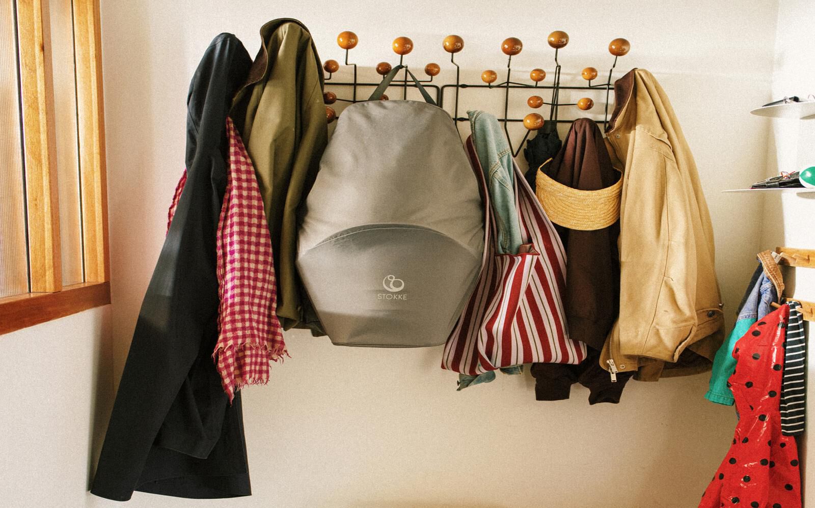 A grey STOKKE YOYO stroller hangs on a coat rack among coats and bags in a hallway.