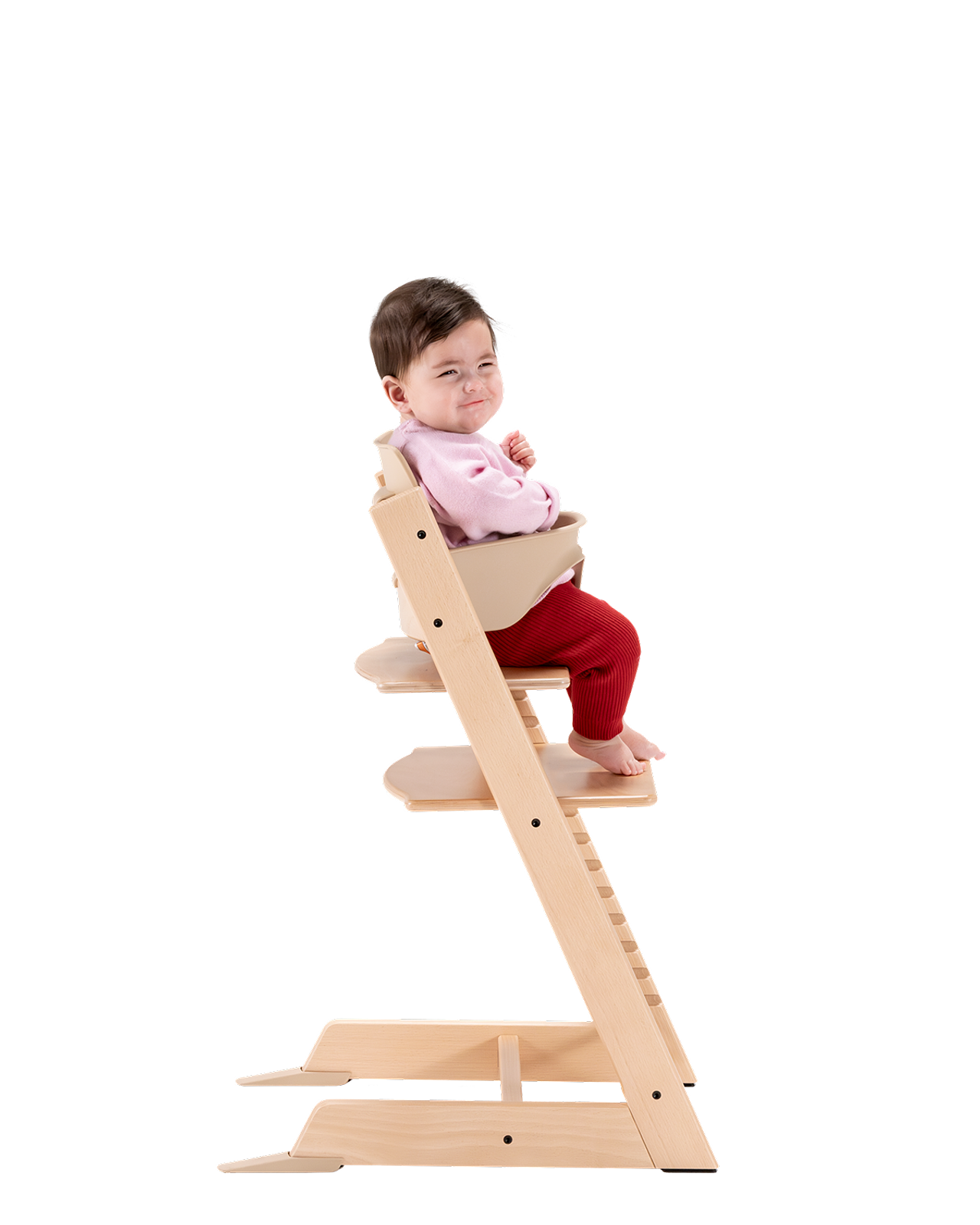 Ein Baby mit einem Grinsen sitzt in einem Tripp Trapp Hochstuhl aus Naturholz mit einem beigefarbenen Baby Set.