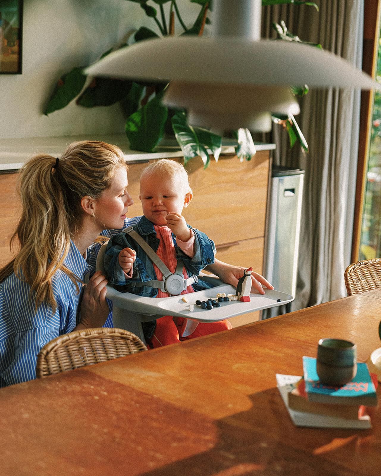 A woman looks lovingly at a baby eating blueberries from a tray in a Tripp Trapp high chair.