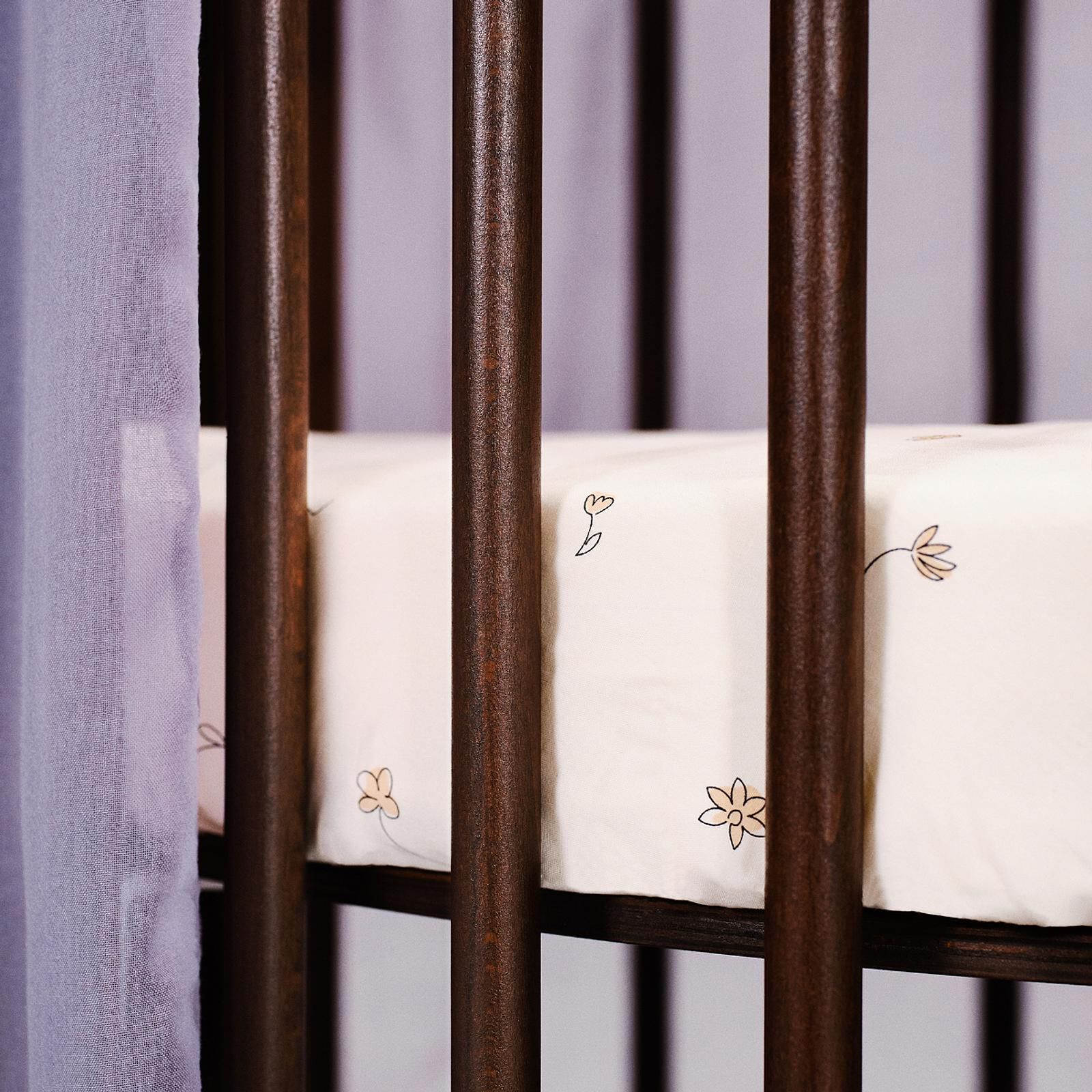 Dark brown wooden crib with a white sheet featuring small flowers, and a purple curtain.