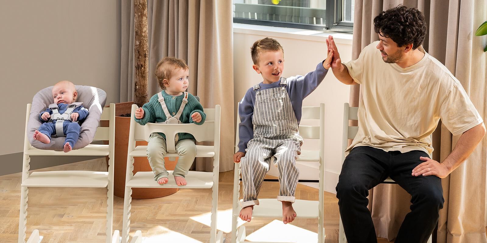 Baby in Tripp Trapp Newborn Set high chair, toddler in Baby Set high chair, child high-fives adult.