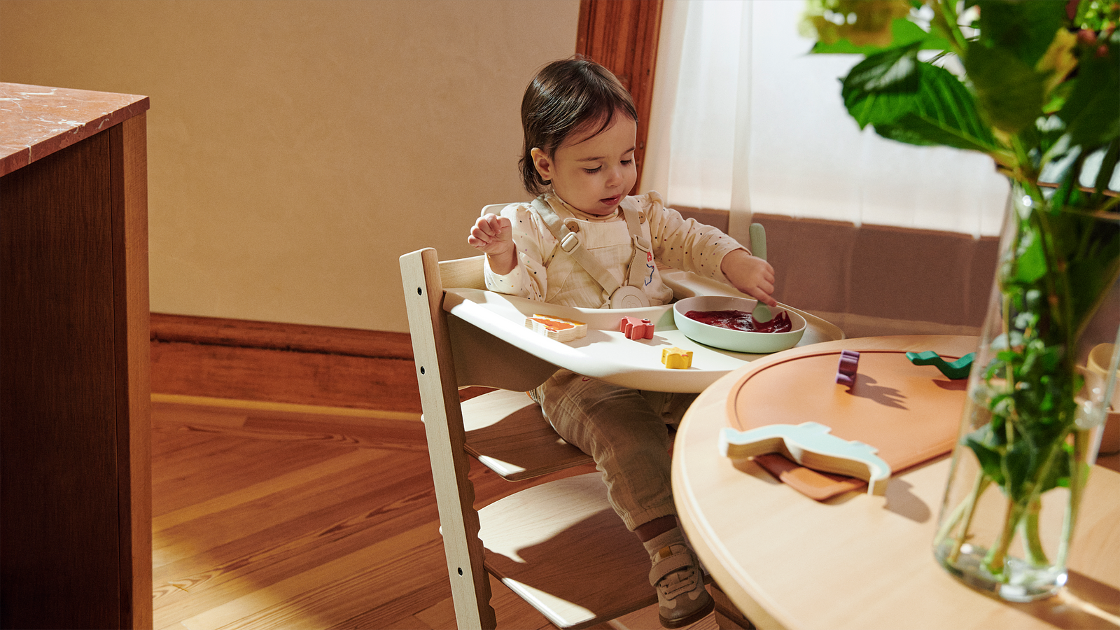 A child in a light wood Tripp Trapp high chair focused on eating from a bowl.