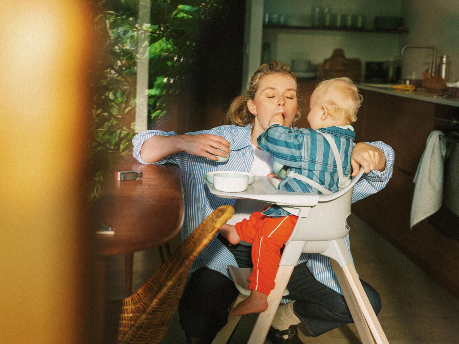 A baby puts its hand in its mother's mouth from a high chair.
