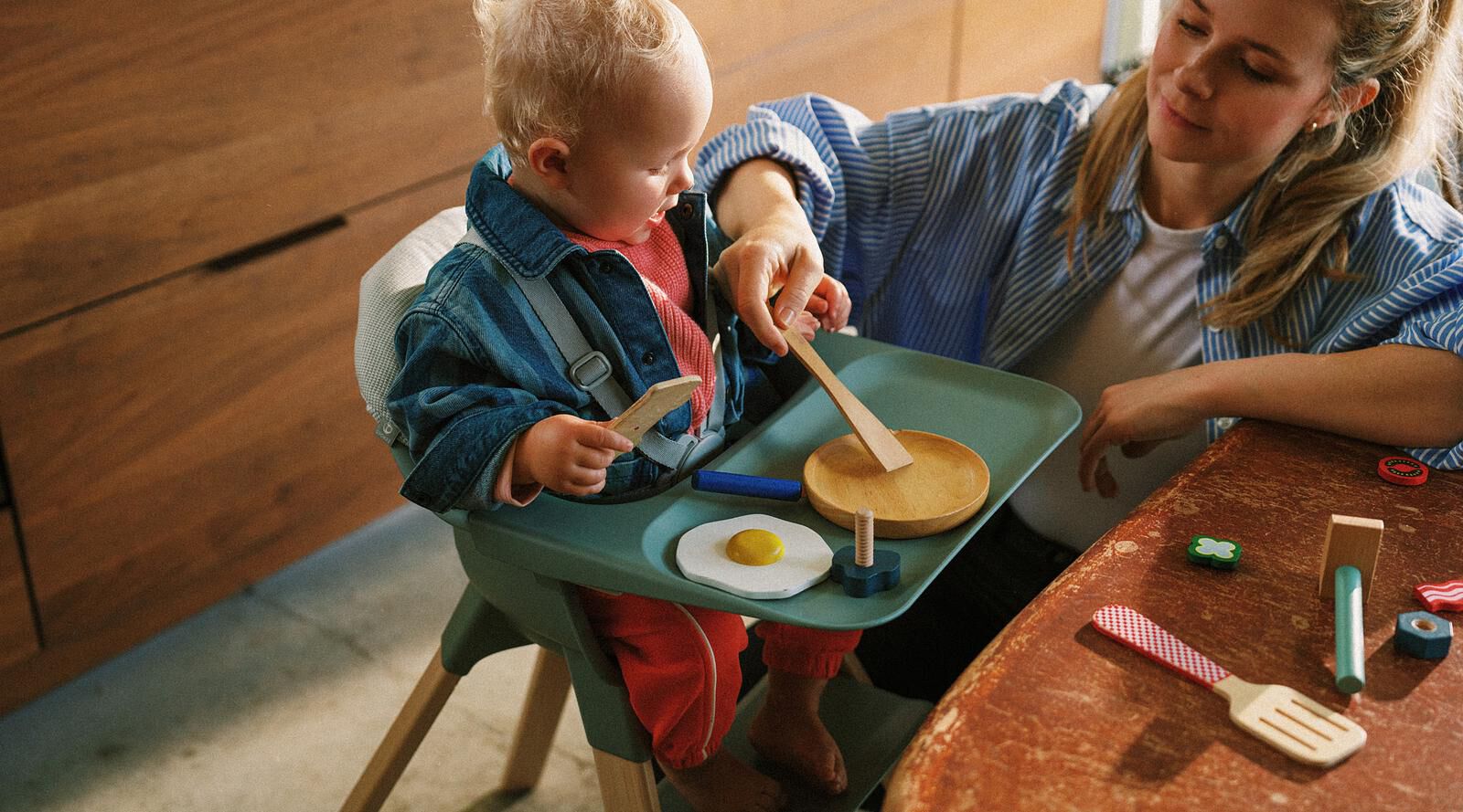 Una mamá y un bebé juegan con comida de juguete en una mesa en una silla alta.
