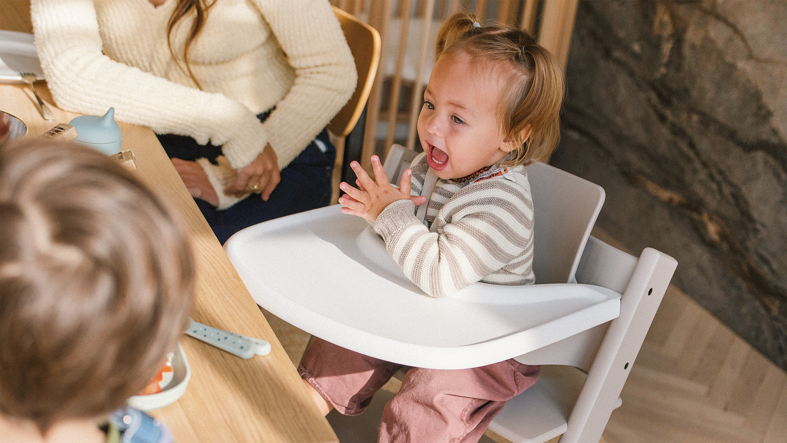 Toddler laughing and clapping in a white Tripp Trapp high chair at a table.