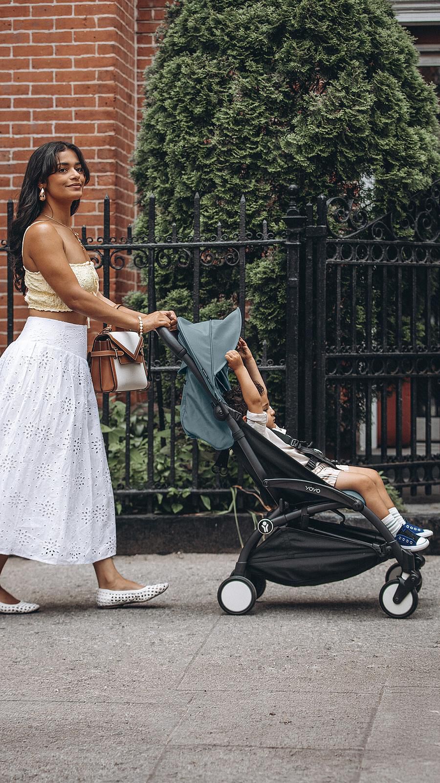 Eine Frau schiebt ein Kind in einem blauen STOKKE YOYO Kinderwagen auf einem Bürgersteig.