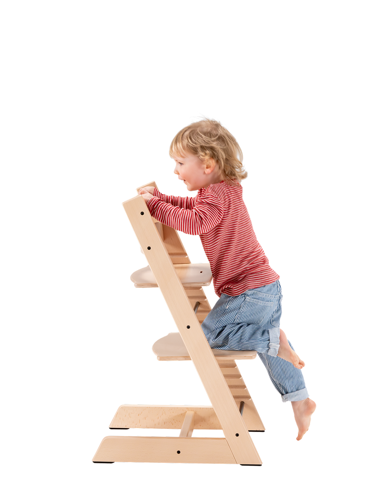 Blonde toddler climbs a light wood Tripp Trapp chair.