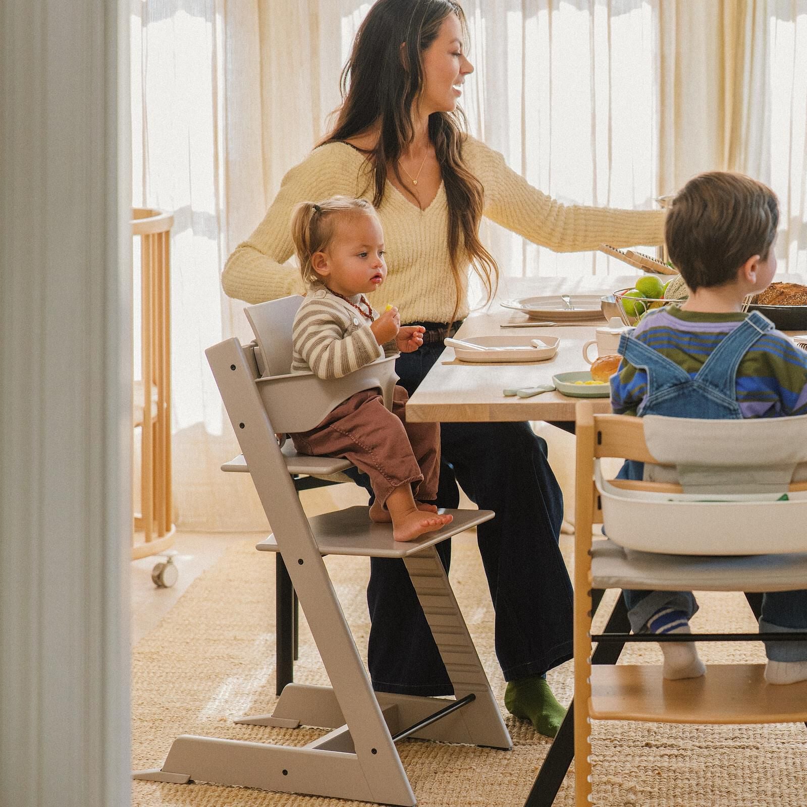Woman and two children eating at table in Tripp Trapp high chairs.
