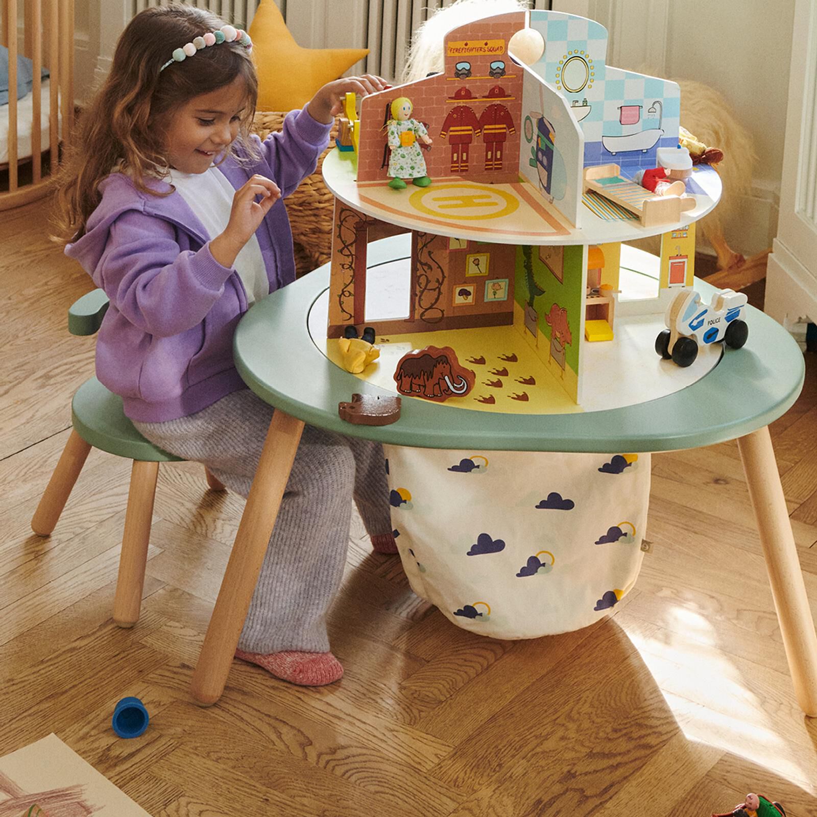 Een meisje speelt met een speelgoedhuis met meerdere kamers op een groene kindertafel met een wolkpatroon opbergtas.