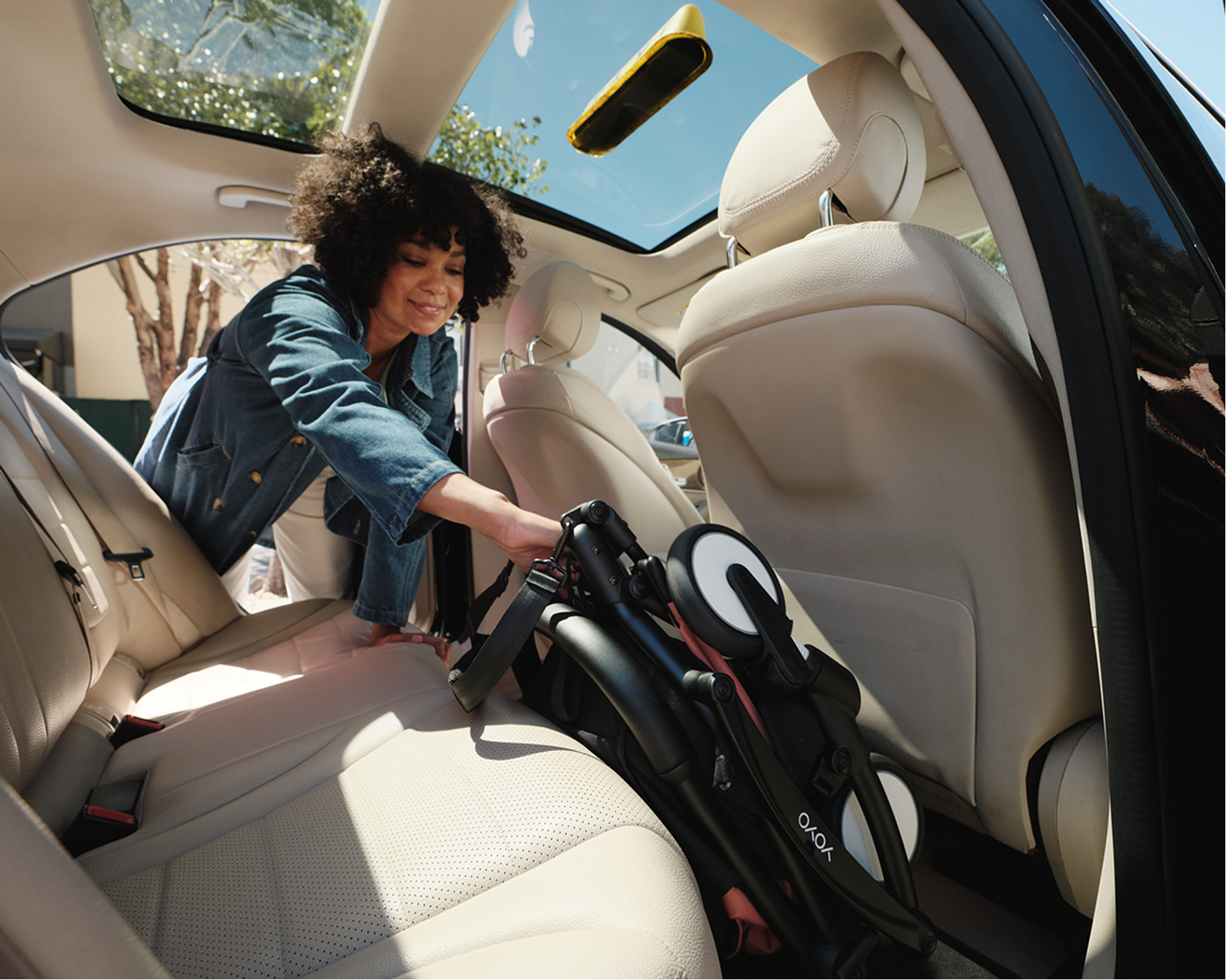 A woman places a folded STOKKE YOYO stroller into the back seat of a car.
