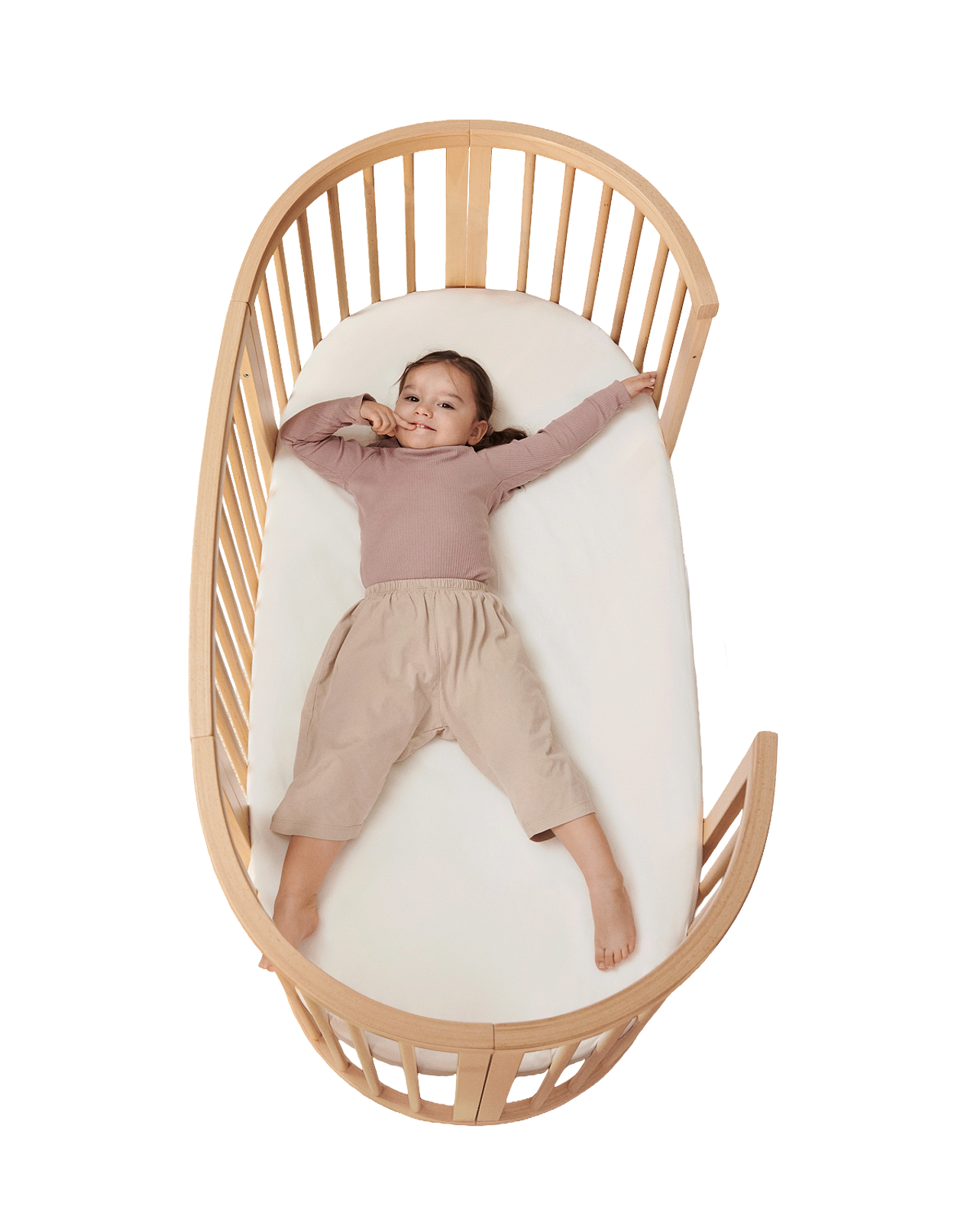 Ett leende barn ligger utsträckt i en STOKKE Sleepi spjälsäng i trä.