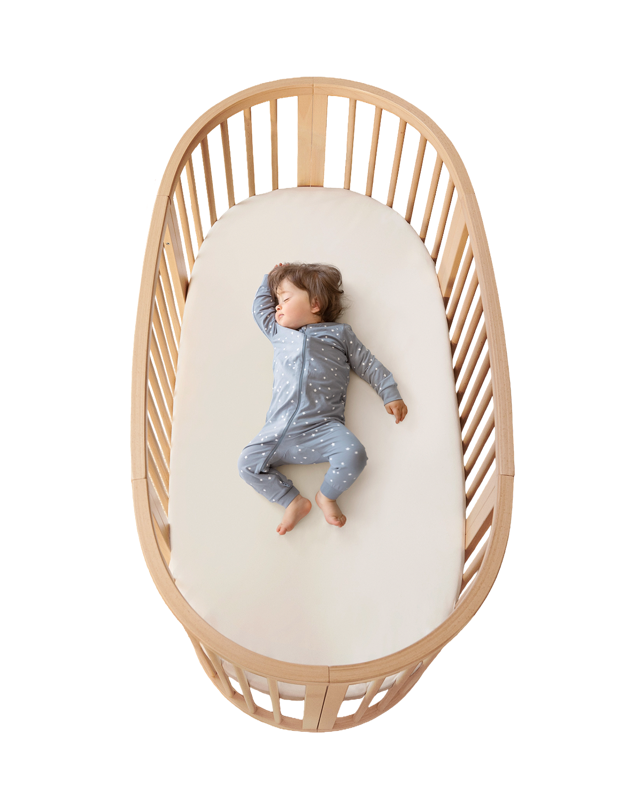 Un bébé en pyjama gris étoilé dort paisiblement sur un matelas blanc dans un berceau ovale en bois.