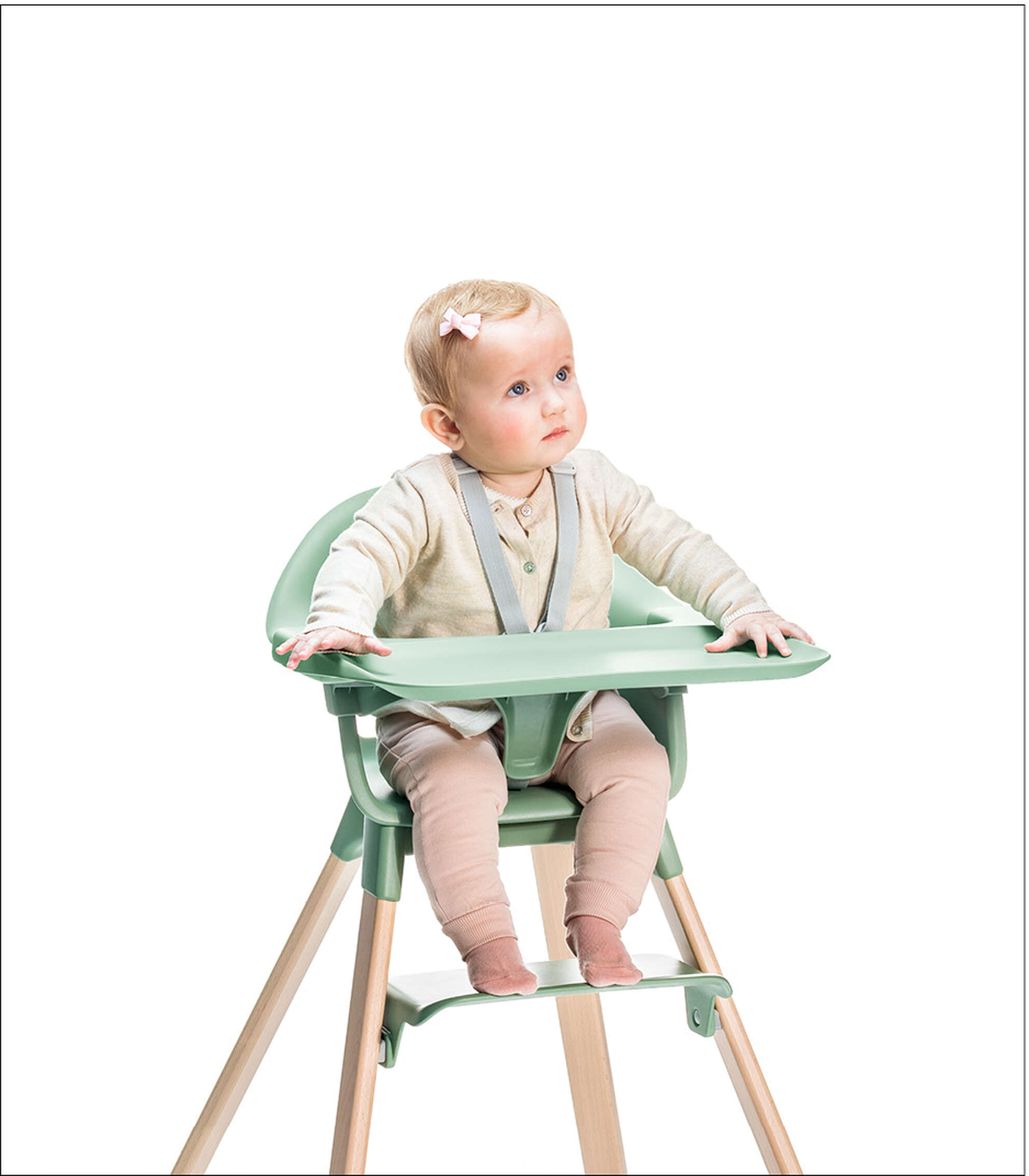 Child sitting in green high chair with tray and safety harness